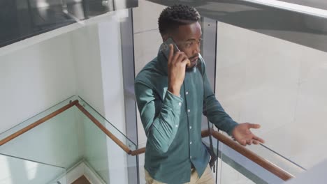 African-american-businessman-talking-on-smartphone-and-walking-in-creative-office