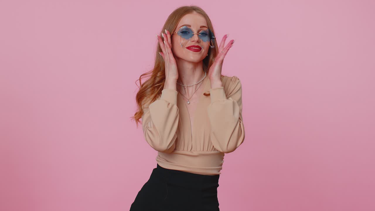 Seductive cheerful brunette girl in beige blouse wearing sunglasses charming smile on pink wall