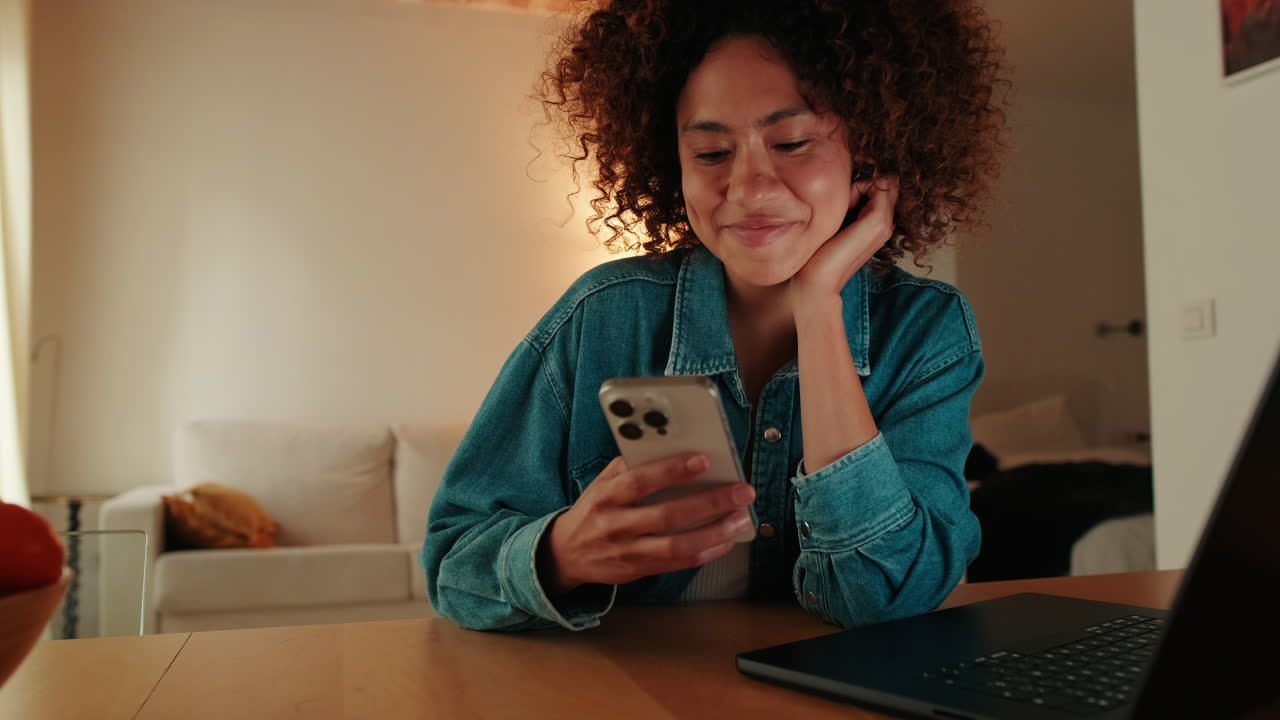 Happy Young Woman Using Smartphone and Smiling at Home