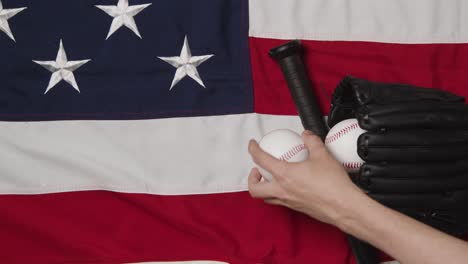 Baseball-Stillleben-über-Dem-Kopf-Mit-Schläger-Und-Fängerhandschuh-Auf-Amerikanischer-Flagge-Mit-Person,-Die-Den-Ball-Aufhebt-1