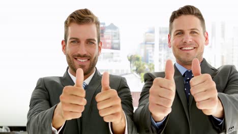 hombres de negocios sonrientes mirando a la cámara dando pulgares hacia arriba