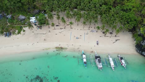 Aerial-pullback-parallax-palawan-beach-with-outrigger-canoes-reveals-mountains