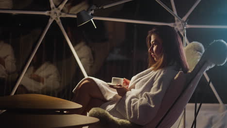 gloomy woman enjoys coffee in dimly lit room relaxing on glamping program. depressive attitude towards life and loneliness. relaxation alone among virgin nature