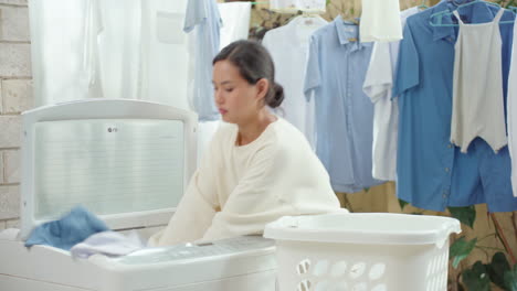 young domesticated woman puts laundry into washing machine from the basket