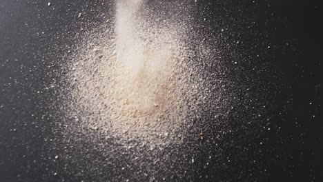 Video-of-close-up-of-sand-grains-pouring-into-heap-and-copy-space-on-black-background