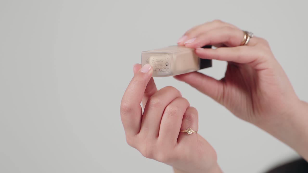 Close up of hands holding a foundation bottle, showcasing product details on a minimalist background