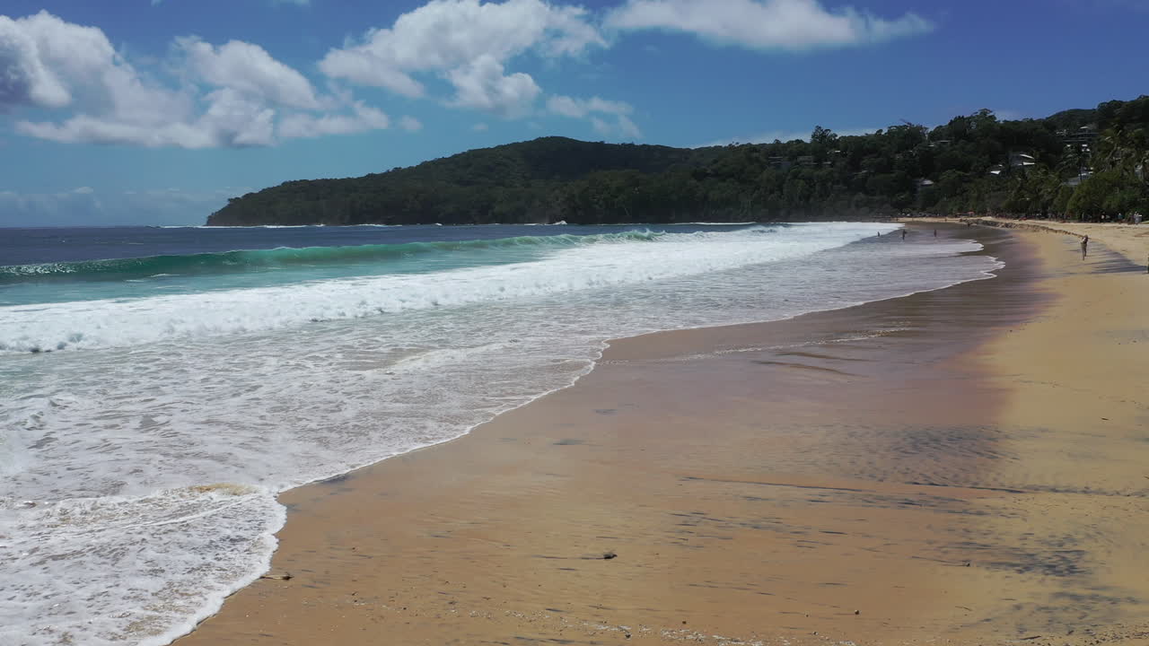 Vista a baja altitud de las olas rompiendo en la playa de Noosa con arena dorada.