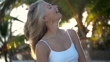 closeup slow motion of backlit mature woman as she throws her hair from side to side and then smiles at camera