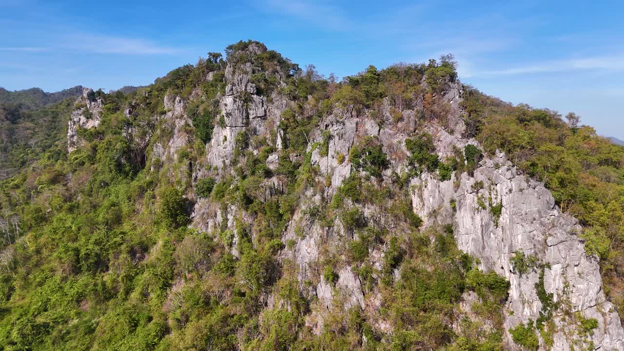 Rekaman drone menangkap formasi batuan kapur dan hutan hijau lebat di bawah langit biru cerah.