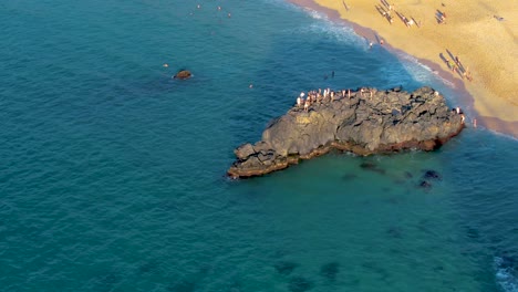 Vista-Aérea-De-La-Multitud-En-La-Cima-De-La-Formación-Rocosa-Saltando-Al-Agua-En-La-Playa-De-La-Bahía-De-Waimea,-Isla-De-Oahu