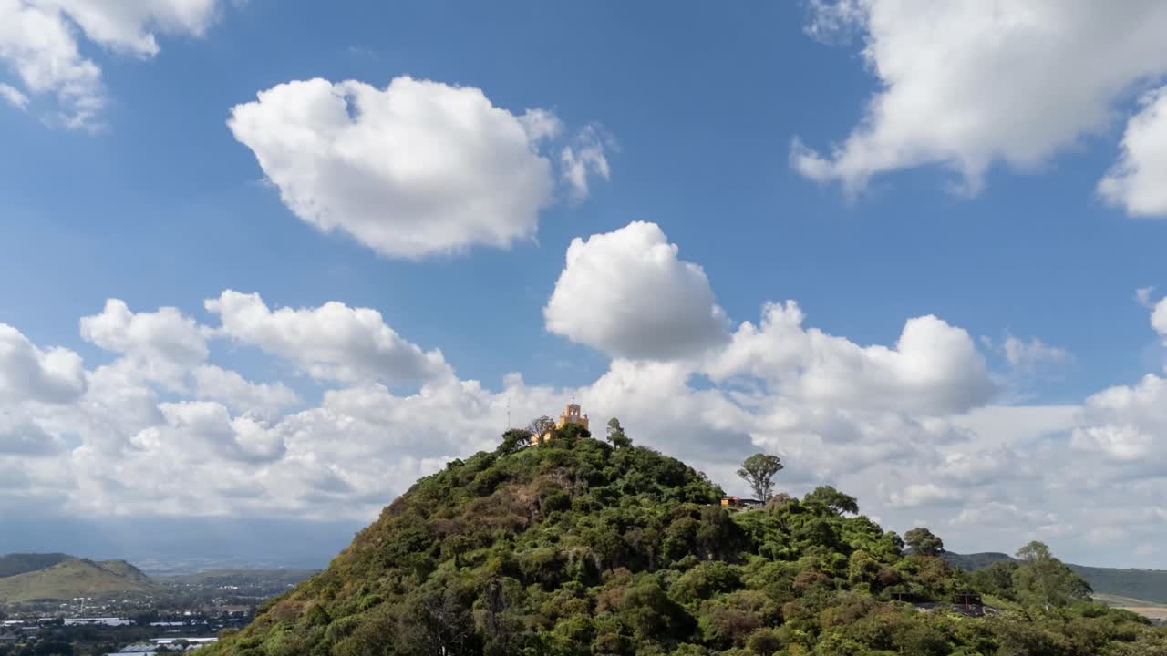 A time-lapse zooms in on Cerro de San Miguel and its chapel, with clouds drifting across the sky.