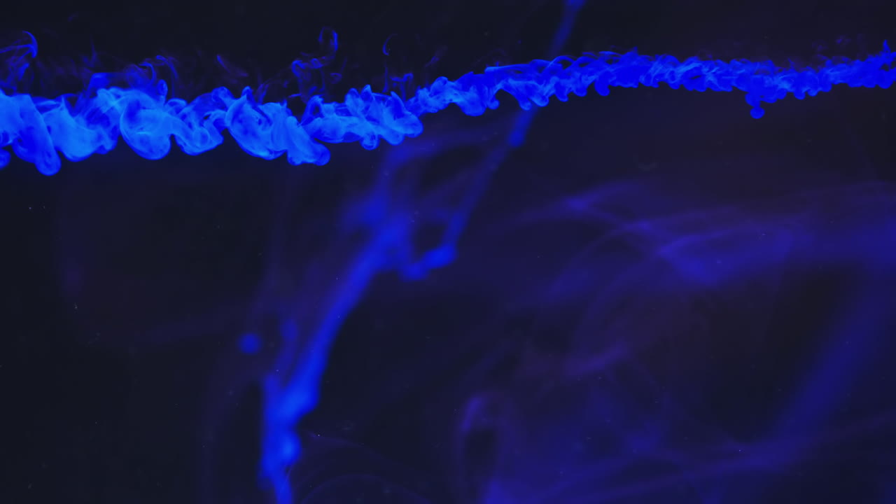 video en cámara lenta de tinta de acuarela azul mezclándose en agua contra un fondo negro