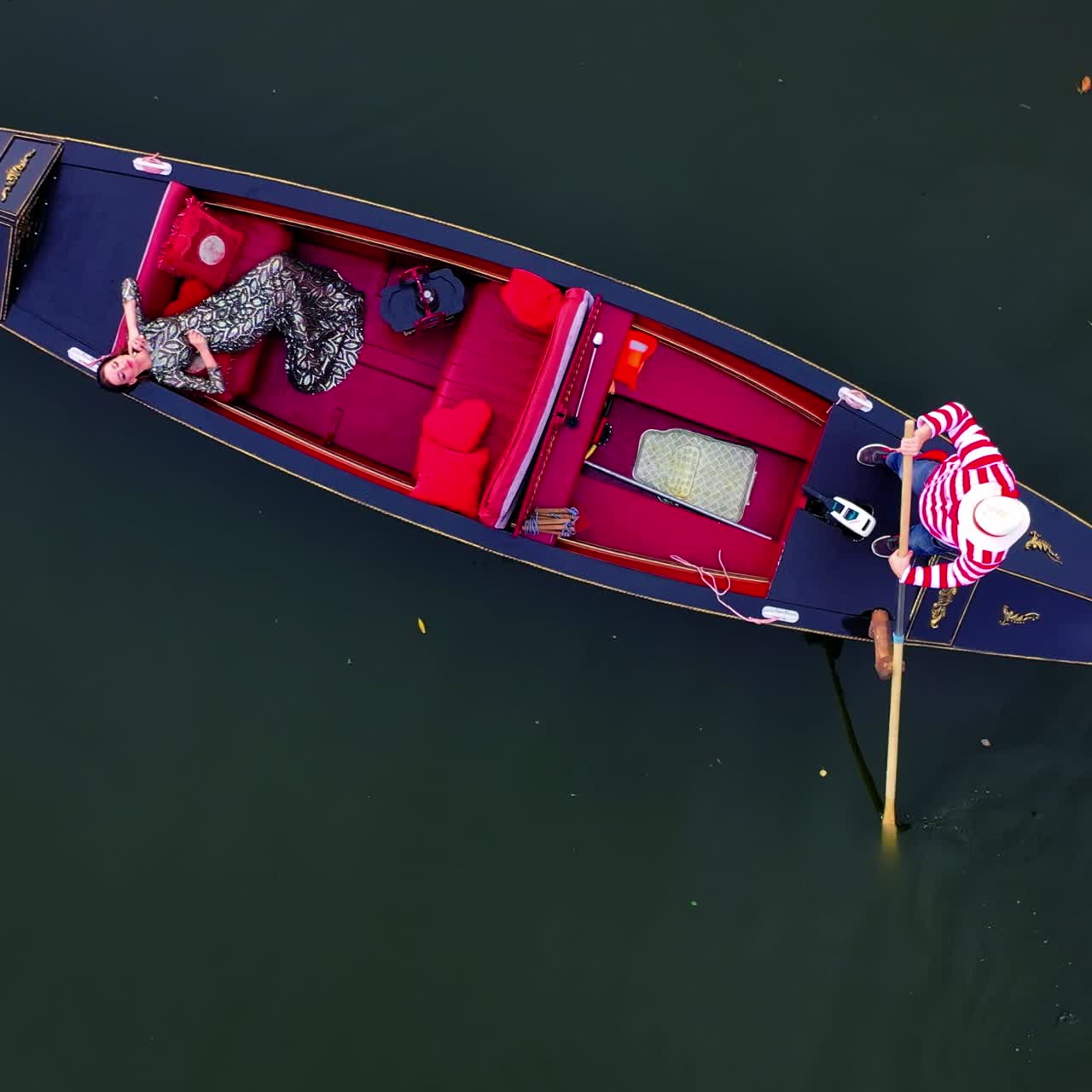 Luxury woman laying in gondola. Pretty girl travels in a boat in Venice. Gondolier managing a gondola on water. Camera rising up.