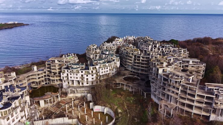 Abandoned coastal complex reveals nature's reclaiming touch by the sparkling sea during a tranquil daylight scene