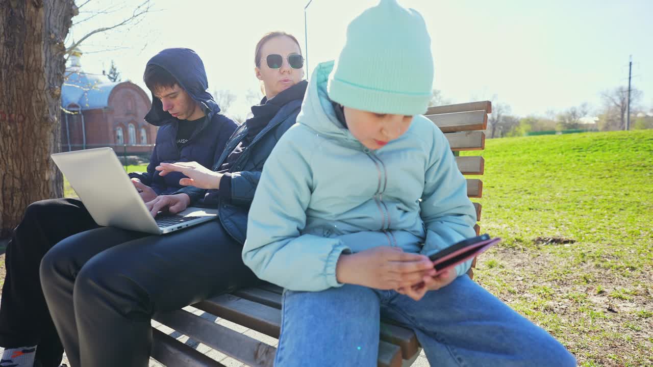 Family Using Digital Devices on a Park Bench on a Sunny Day