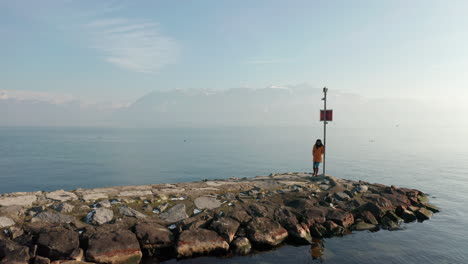 aerial dolly of woman standing at the edge on stone quay at lake geneva, switzerland