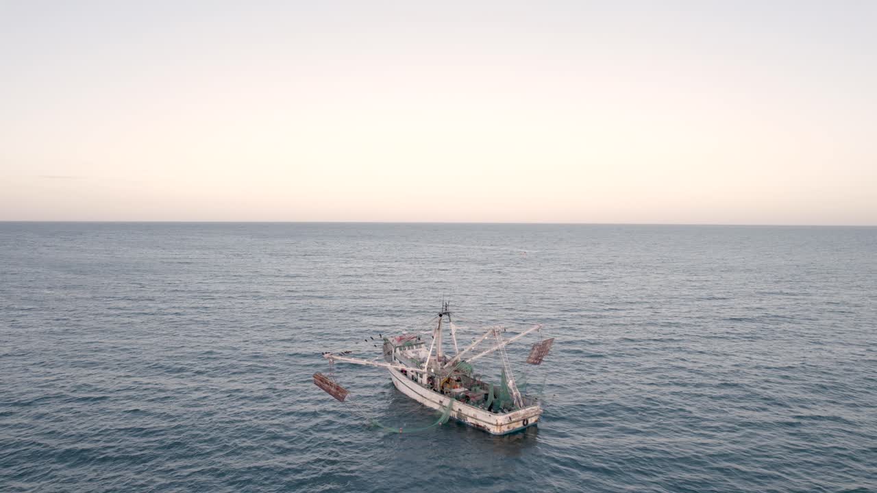 Ripresa aerea con drone che circonda un peschereccio di gamberi mentre pesca al tramonto