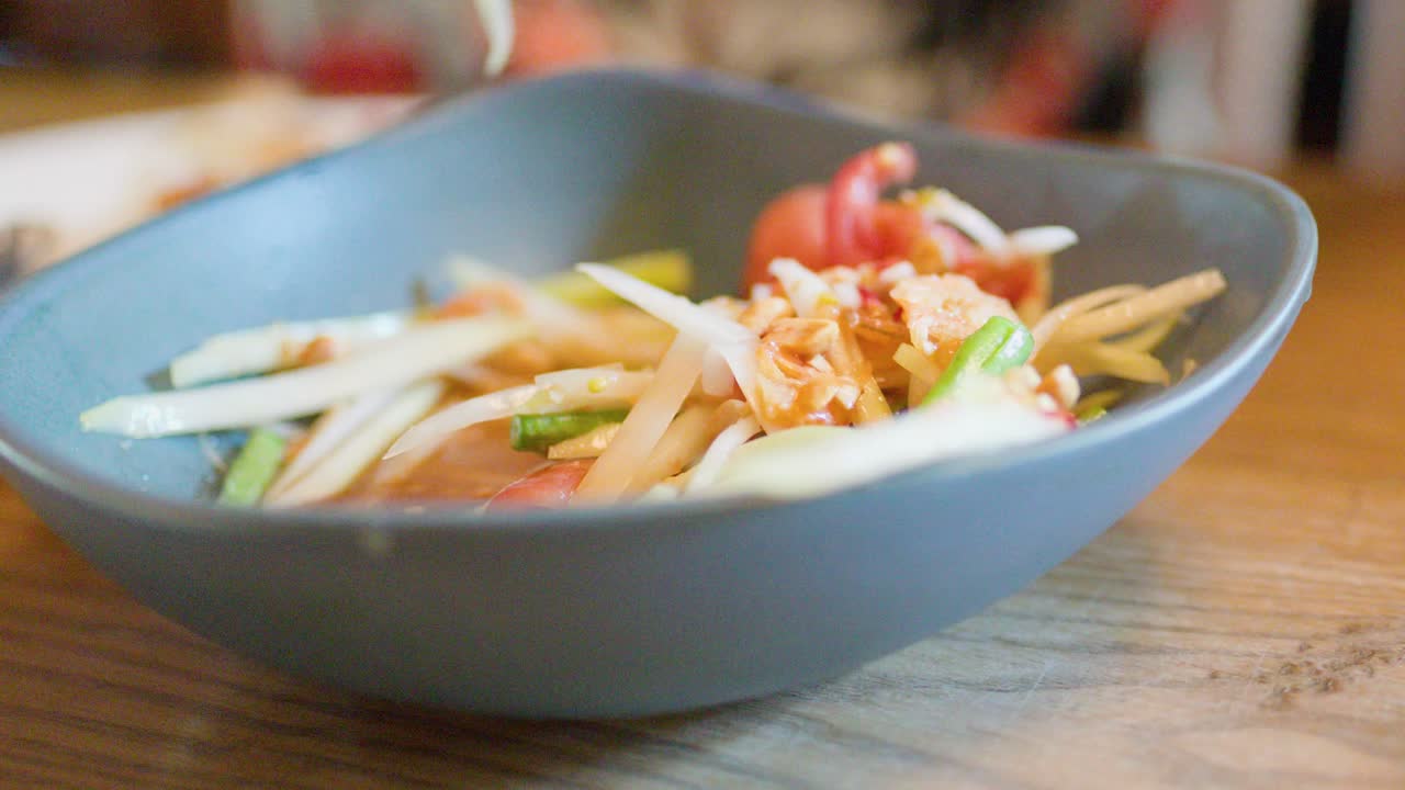 Hand scooping spicy green papaya salad from bowl, natural lighting, shallow depth of field