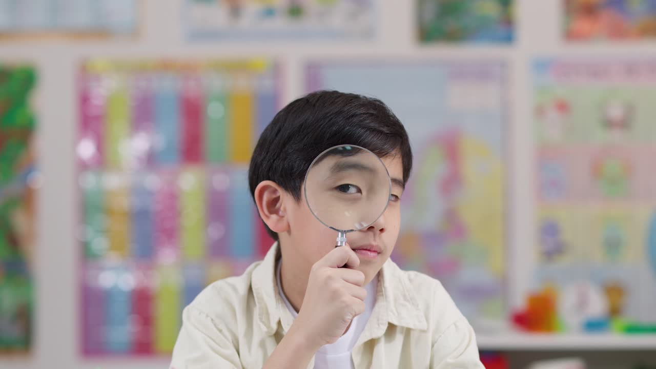 Young boy playfully inspects surroundings with magnifying glass in brightly lit classroom setting