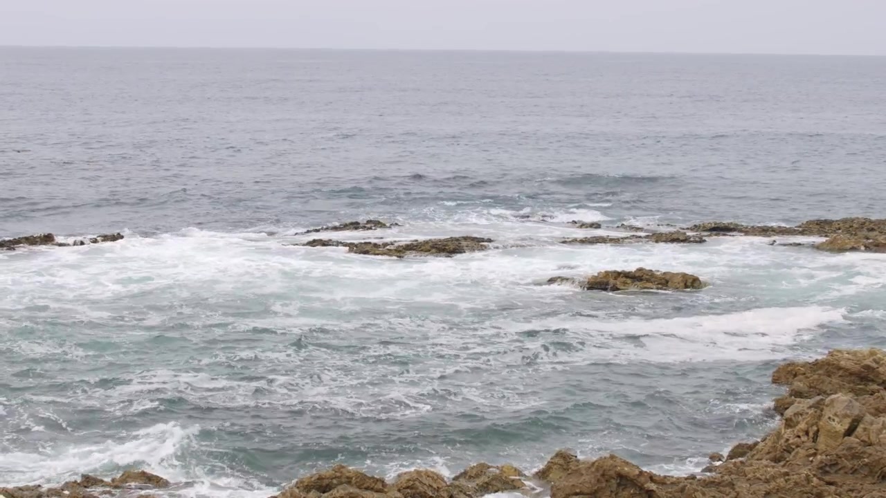 Ombak Samudra Pasifik yang Dramatis Menghantam Garis Pantai Berbatu Terjal di Bawah Awan Mendung Gelap dan Cuaca Murung.