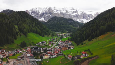 Drone footage of a wide mountain valley surrounded by forested slopes and distant snowy peaks in the Dolomites, Italy