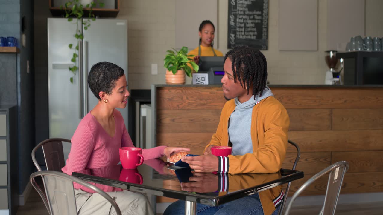 Mid adult woman carrying croissant plate across cafe toward couple at metal table explaining order