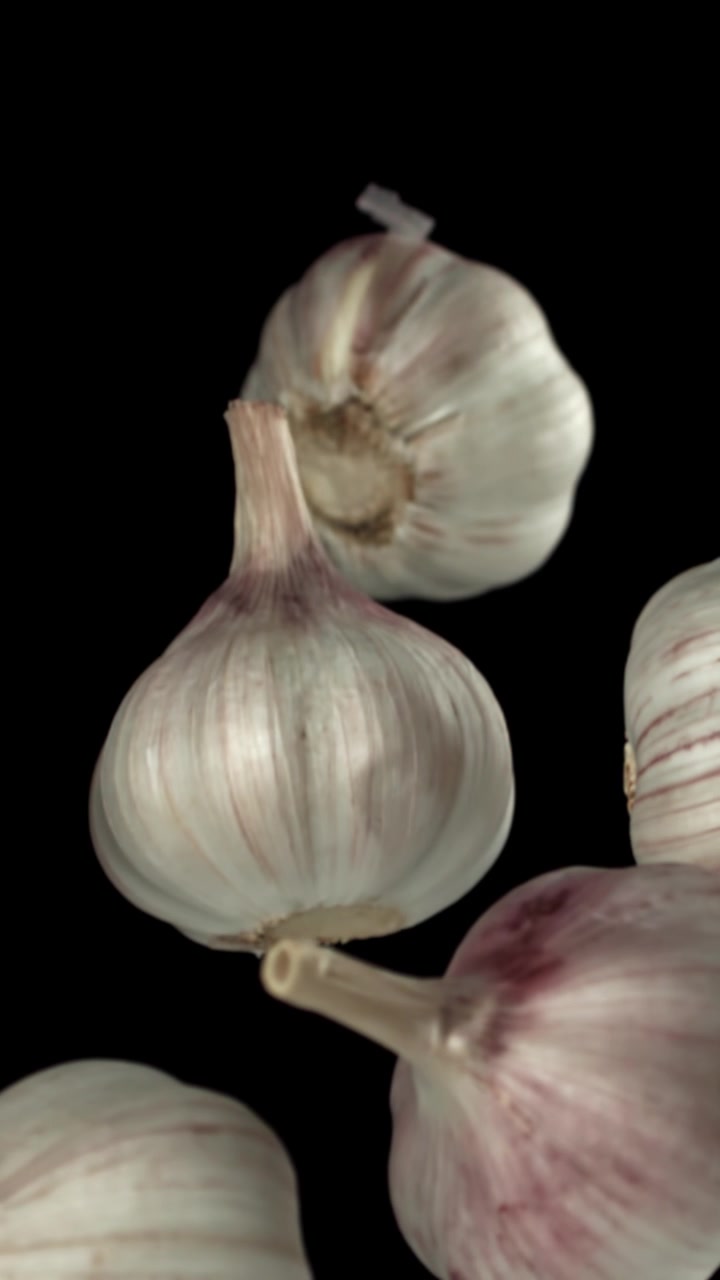 Bulbi d'aglio freschi che salgono lentamente su uno sfondo nero
