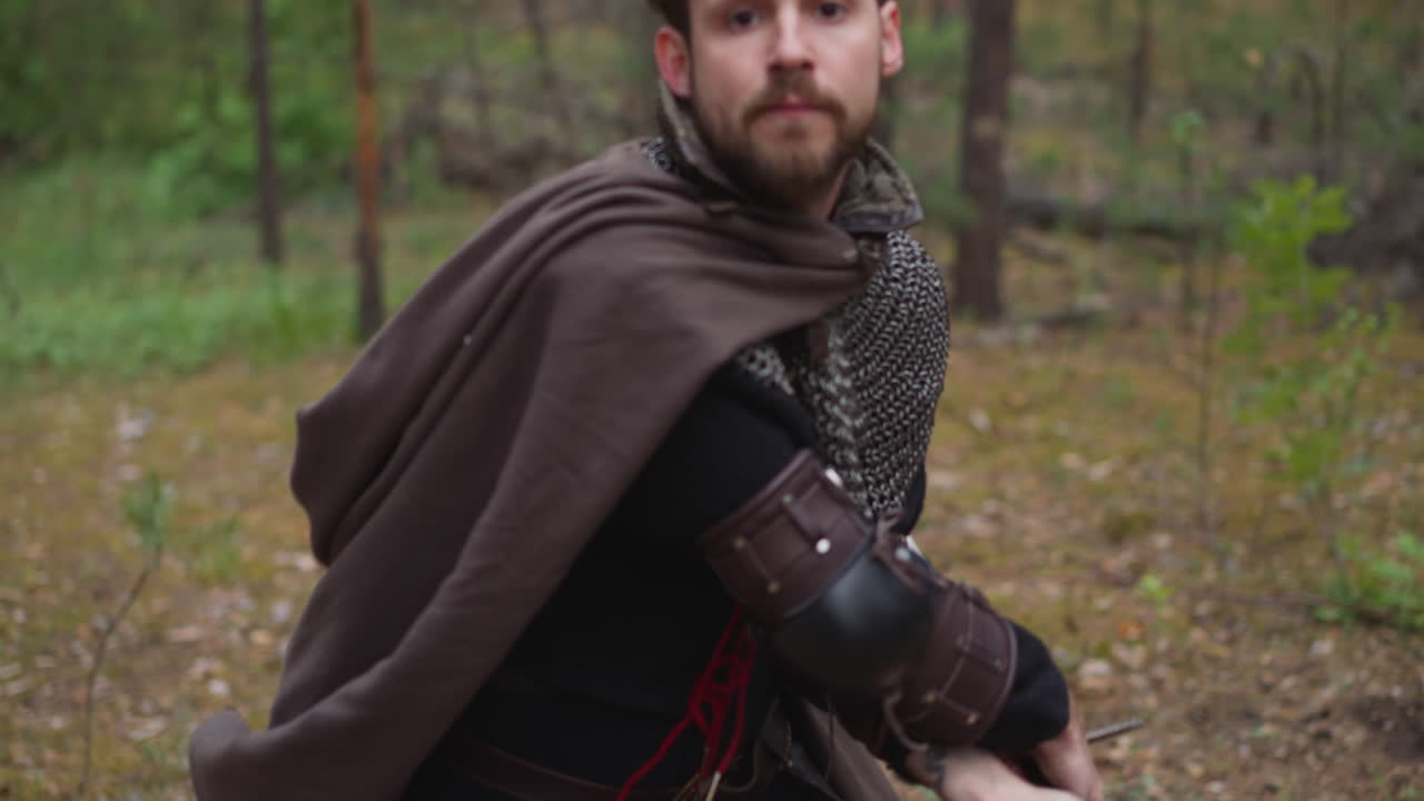 сильный рыцарь с почтой и плащом бьет мечом в лесу