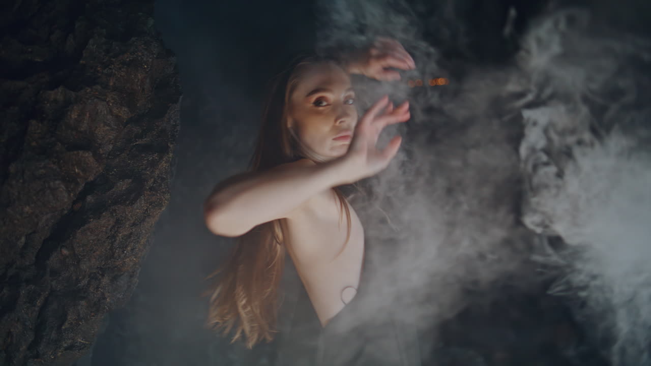 bailarina disfruta de la fiesta de humo cerca de las rocas por la noche retrato. mujer seductora bailando