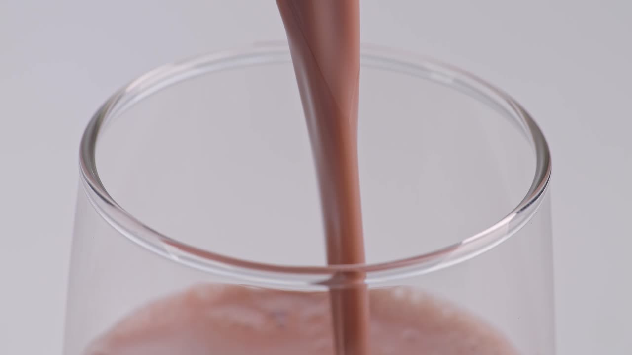Primo piano di bevanda al latte al cioccolato versata al rallentatore in un bicchiere tumbler su sfondo bianco