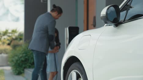 progressive dad and daughter charging ev car from home charging station.