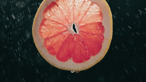 rodaja de pomelo fresco salpicada por niebla de gotas de agua en cámara lenta con fondo negro retroiluminado