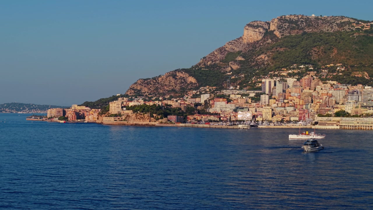 Barca che si muove su acqua blu calma con la città di Montecarlo e le colline sullo sfondo.