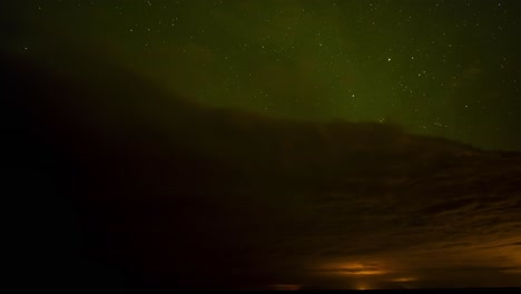 beautiful time lapse of green northern lights above dark clouds with a starry night sky with shooting stars