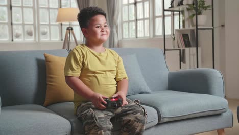 child gamer sitting on a couch, playing and winning games on a console, he plays with a wireless controller