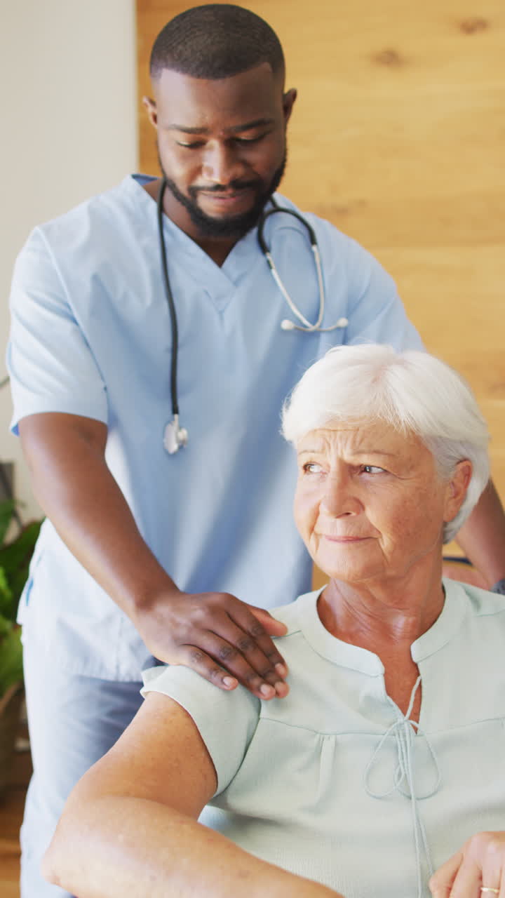 Vertical video of happy african american male physiotherapist exercising with senior patient