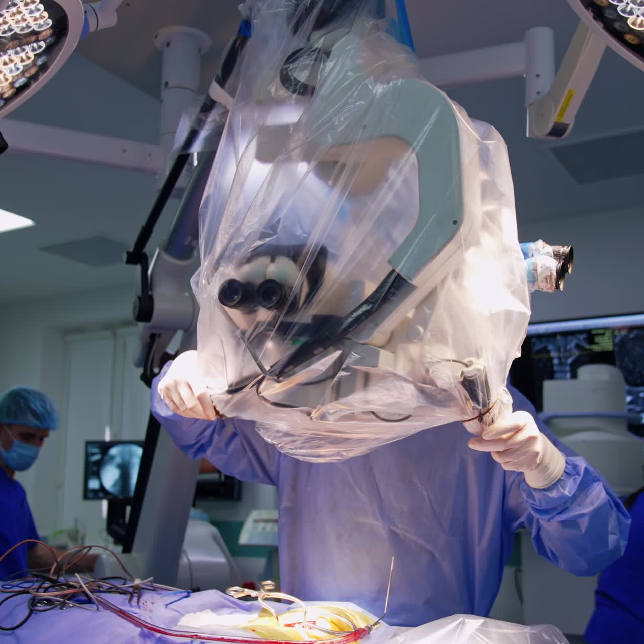 Unrecognized doctor standing behind the powerful microscope hanging over the patient on operational table. Surgical room for neurological operations in hospital
