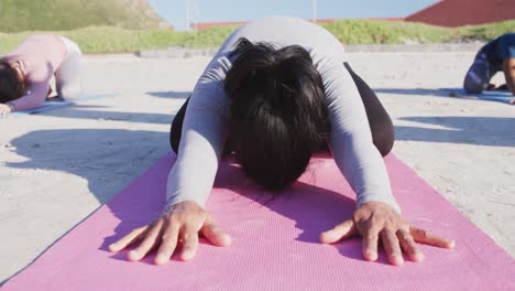 grupo multiétnico de mujeres haciendo posición de yoga en la playa y fondo de cielo azul