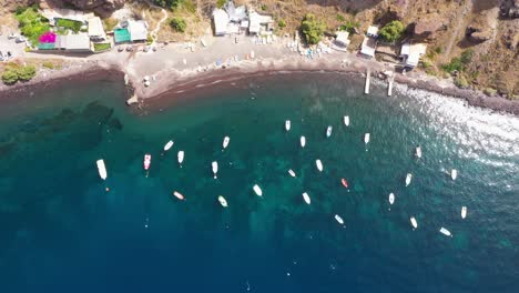 luftaufnahme von oben nach unten auf viele fischerboote im mittelmeer mit kristallklarem, blauem wasser und strand in santorini, griechenland