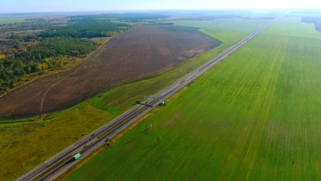 Sky-view-cars-drive-along-highway-past-green-fields.-Car-traffic.-Cars-driveway