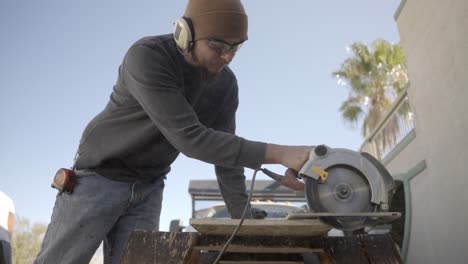 Carpenter-cutting-through-plank-with-circular-saw,-slow-motion-side-view