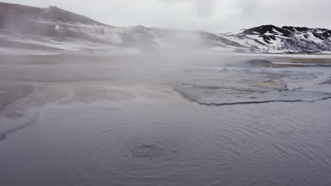 Dark-blue-boiling-mud-pool-with-steam-in-Icelandic-mountain-landscape