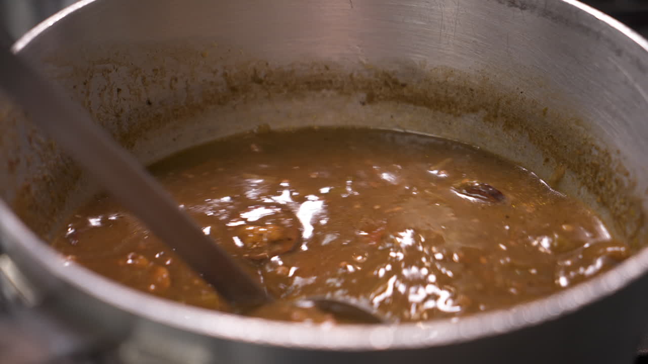 Ladle stirs chicken sausage gumbo, traditional Louisiana cajun dark roux gumbo, close up slow motion 4K