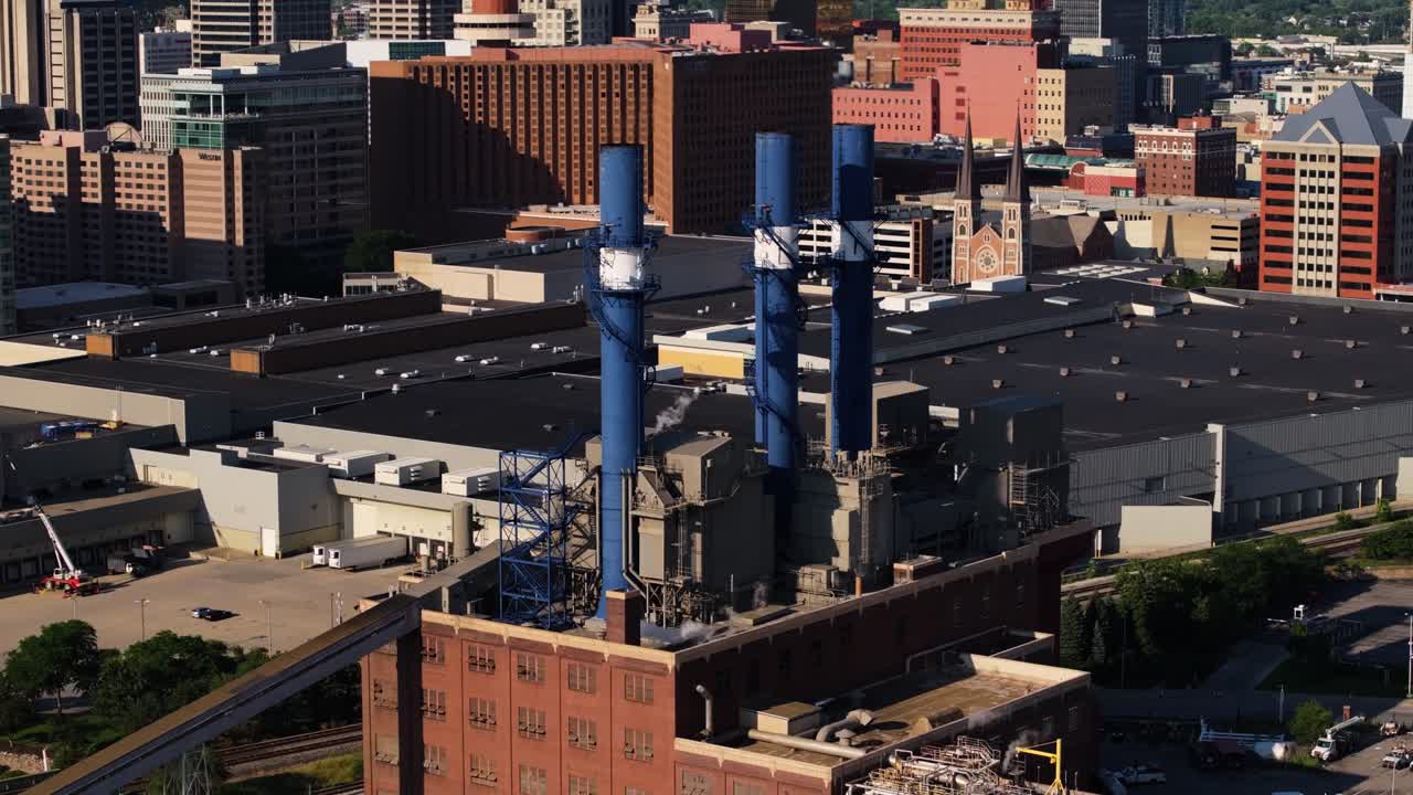 High angle drone shot captures industrial power station in Indianapolis, Indiana with downtown buildings and steam towers in the background