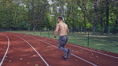 male sprinter training for race. back view of athlete without shirt starting running at outdoor athletics track and field stadium. sport and fitness concept.