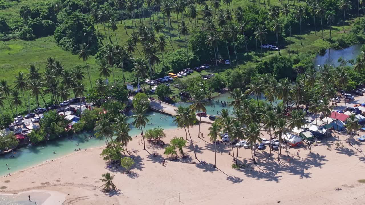 Tropical clear ARROYO SALADO River with coconut trees and resting people during sunny day. Houses and tourist at sandy beach. Aerial top down shot.