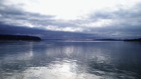 Contrast-of-dark-skies-and-bright-reflections-on-calm-water,-Puget-Sound,-Washington,-aerial
