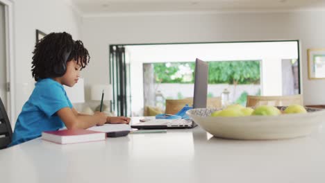 Feliz-Niño-Birracial-Sentado-En-La-Mesa-Usando-Una-Computadora-Portátil-Y-Teniendo-Clases-En-Línea