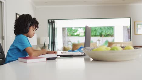happy biracial boy sitting at table using laptop and having online classes
