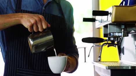 camarero vertiendo leche en el café en el mostrador